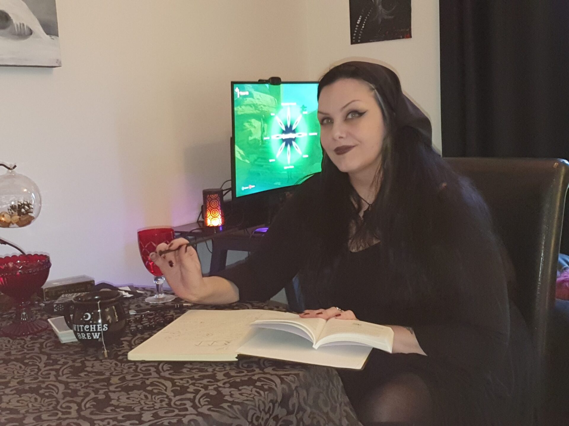Lena sitter ved et bord med en åpen bok foran seg, med PC-skjerm og mørk innredning i bakgrunnen.