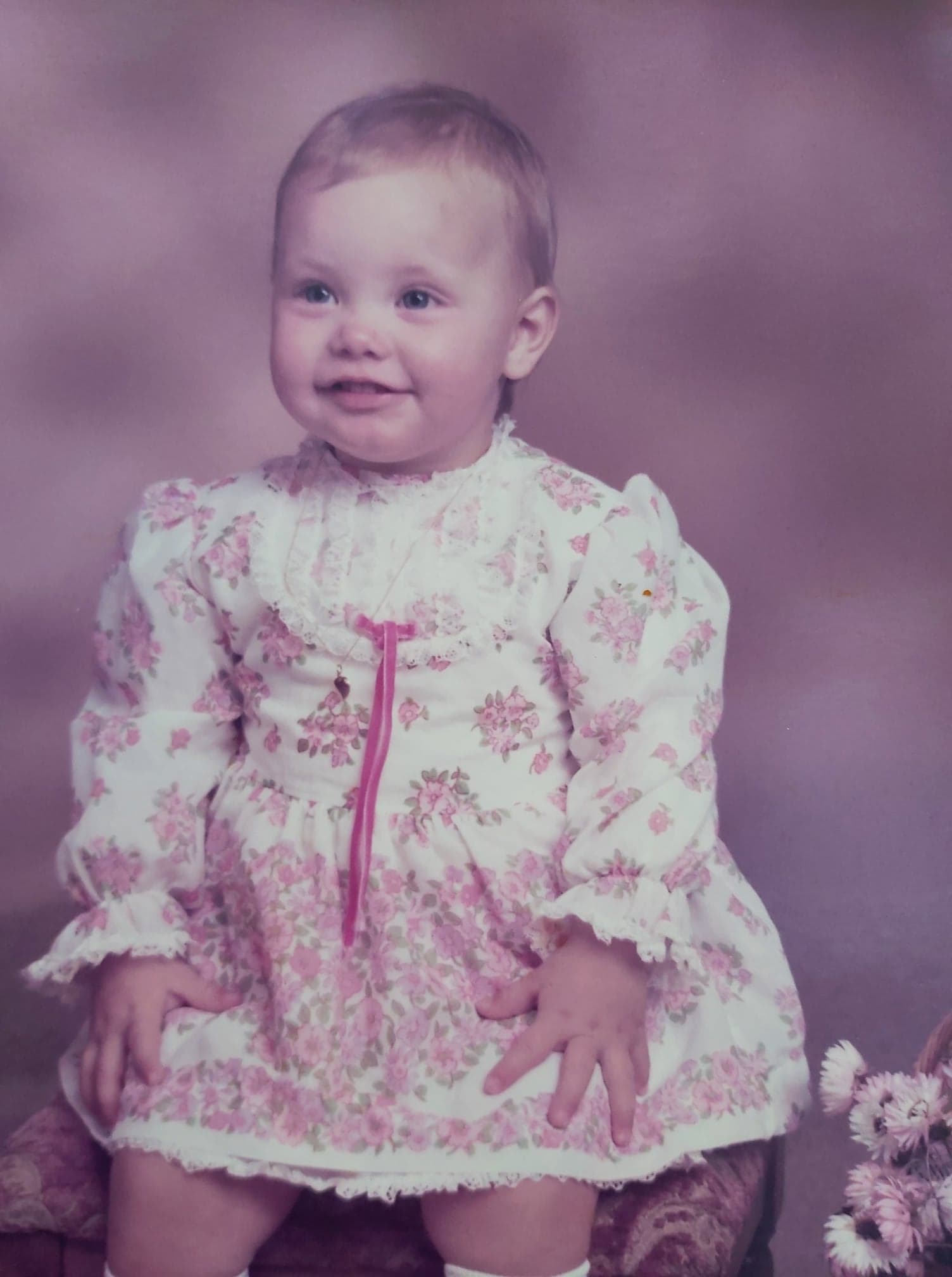 Lena som liten, iført en lys kjole med rosa blomster