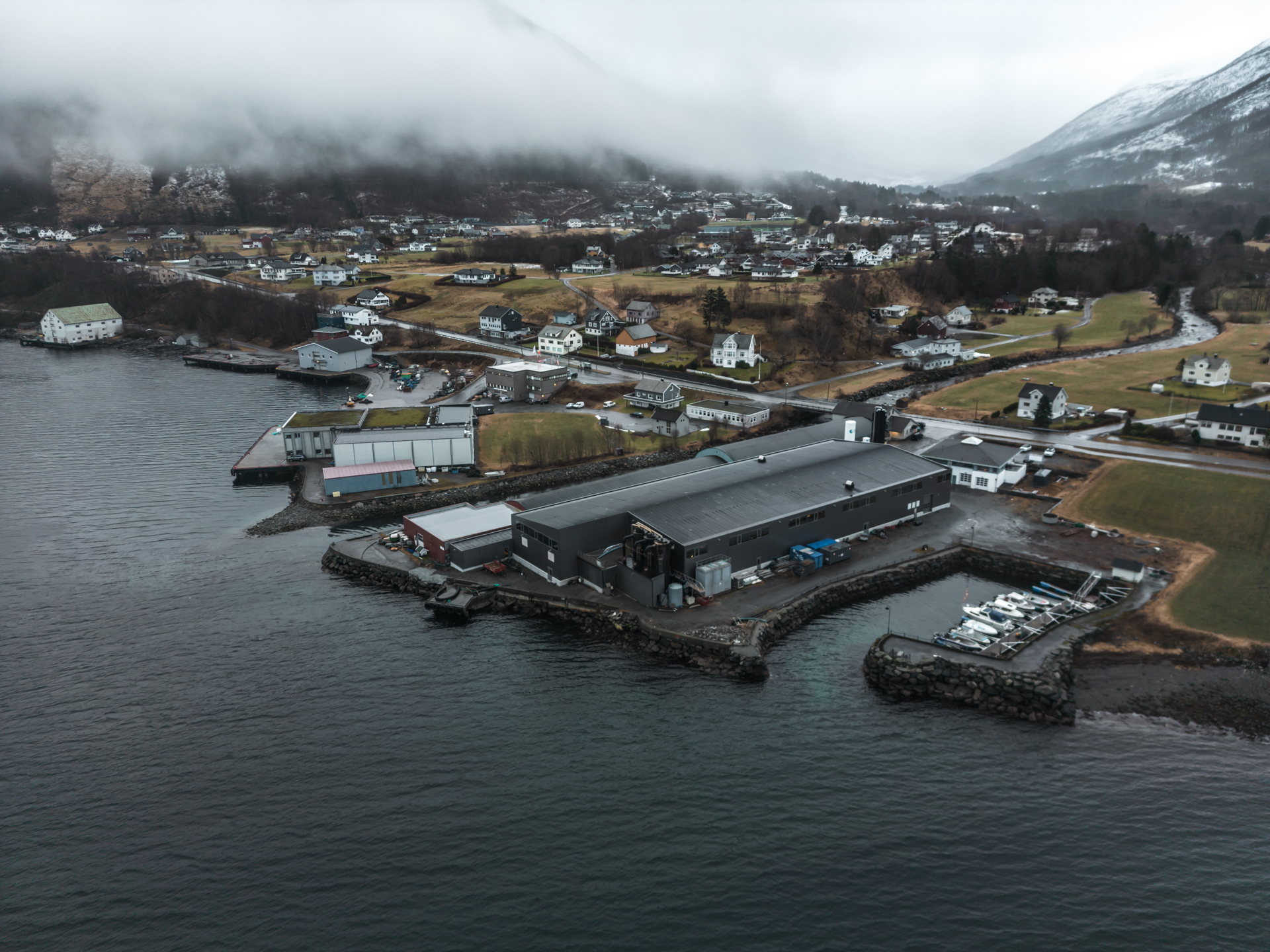 Foto av fiskeoppdrett mot fjorden sett fra lufta