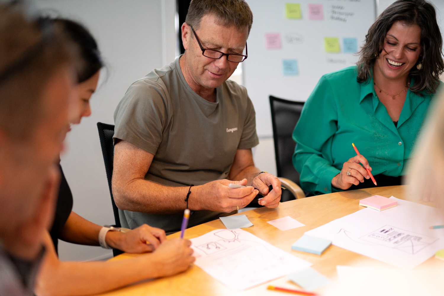 Workshop med arbeidstegninger på bordet. Tre designere sitter å diskuterer et prosjekt