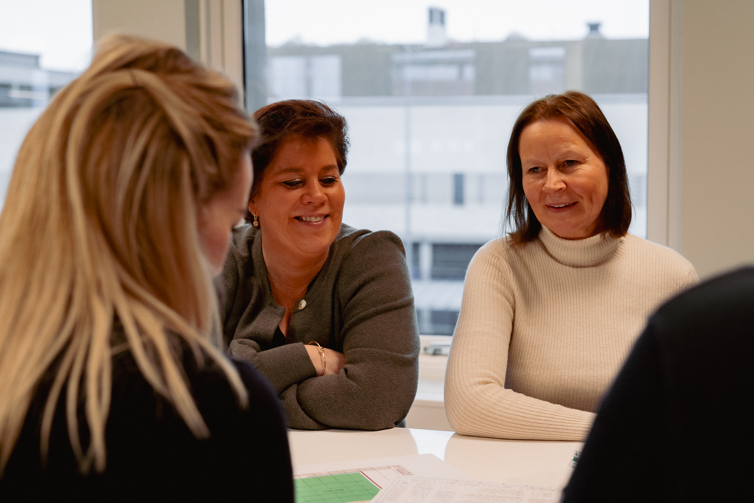 Tre ansatte i Arena Service Team ler sammen rundt et møtebord