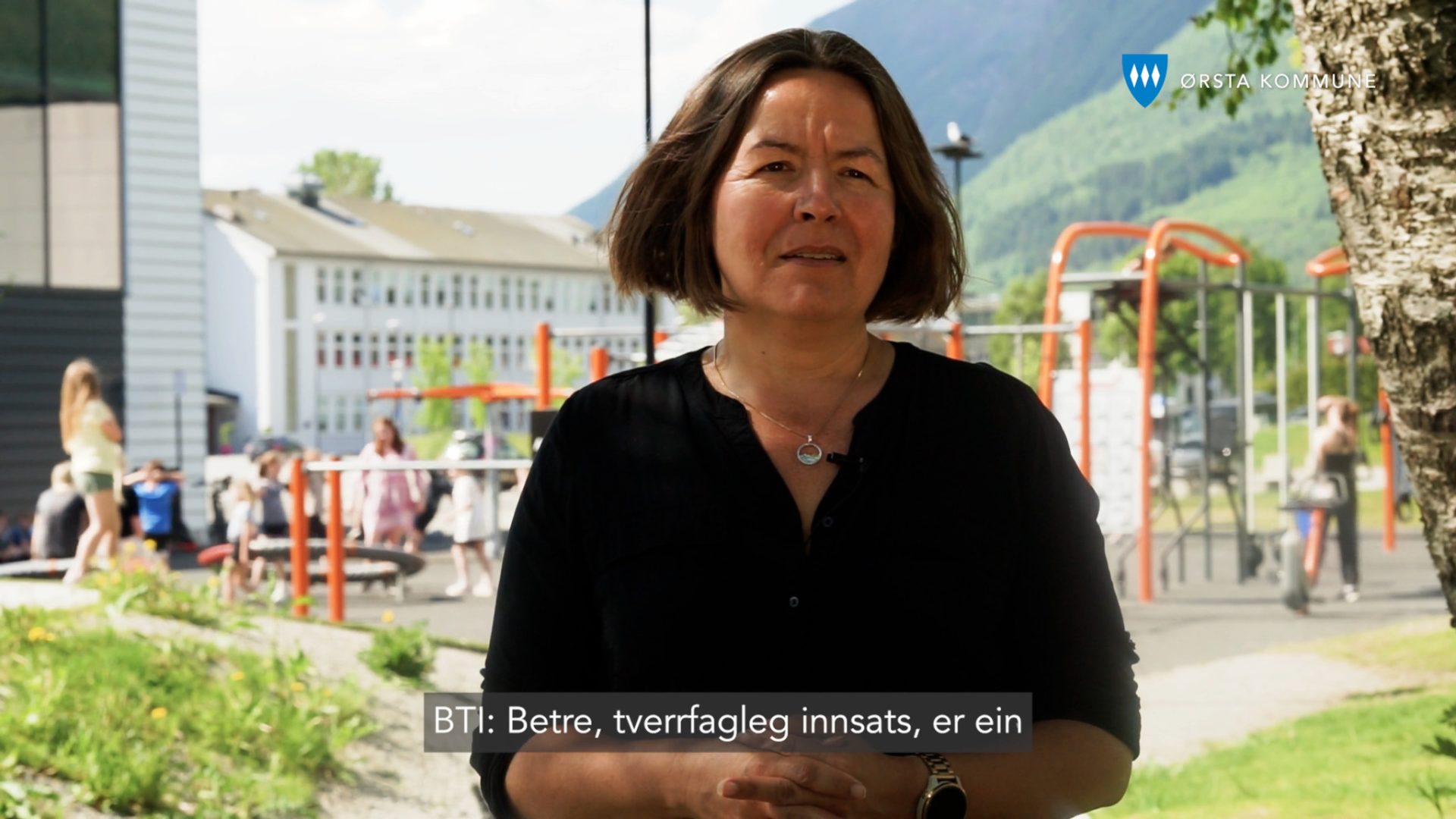 Ansatt i Ørsta kommune som snakker om bedre tverrfaglig innsats, med barn som leker i bakgrunnen.