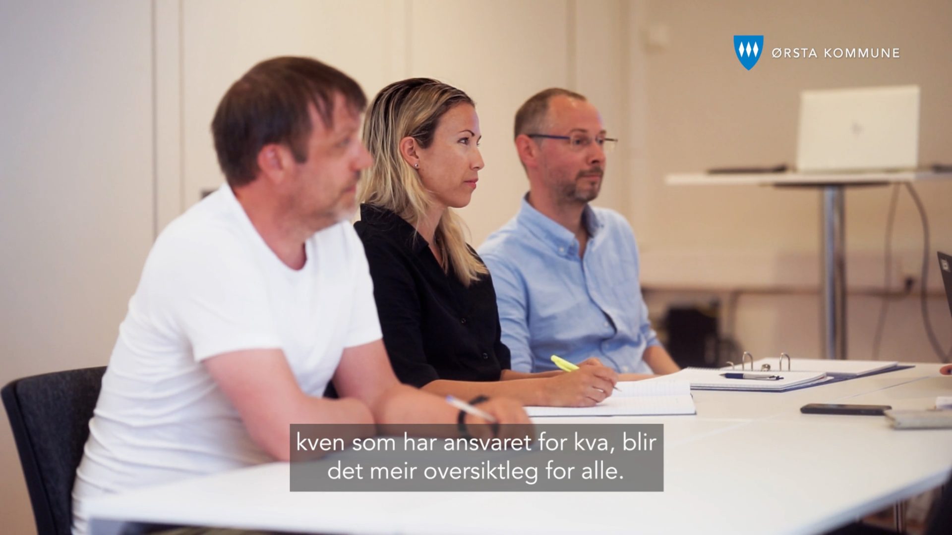 Tre ansatte ved et møtebord under en samtale om ansvar og oppfølging.