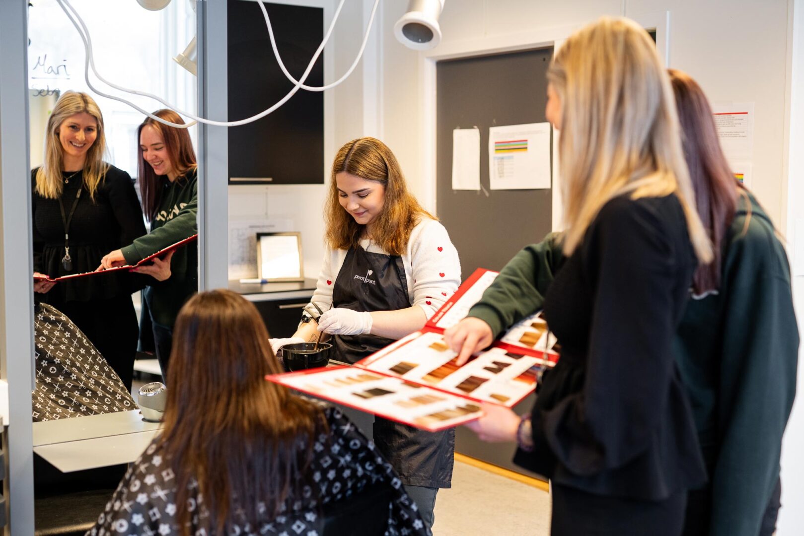 Frisørelever som arbeider med hårbehandling og diskuterer frisyrer i en salong.