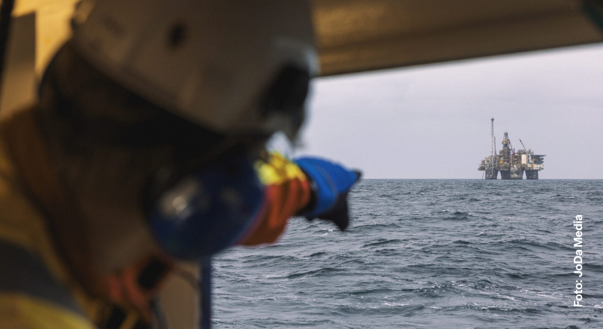 Offshorearbeider som peker mot en installasjon til havs.