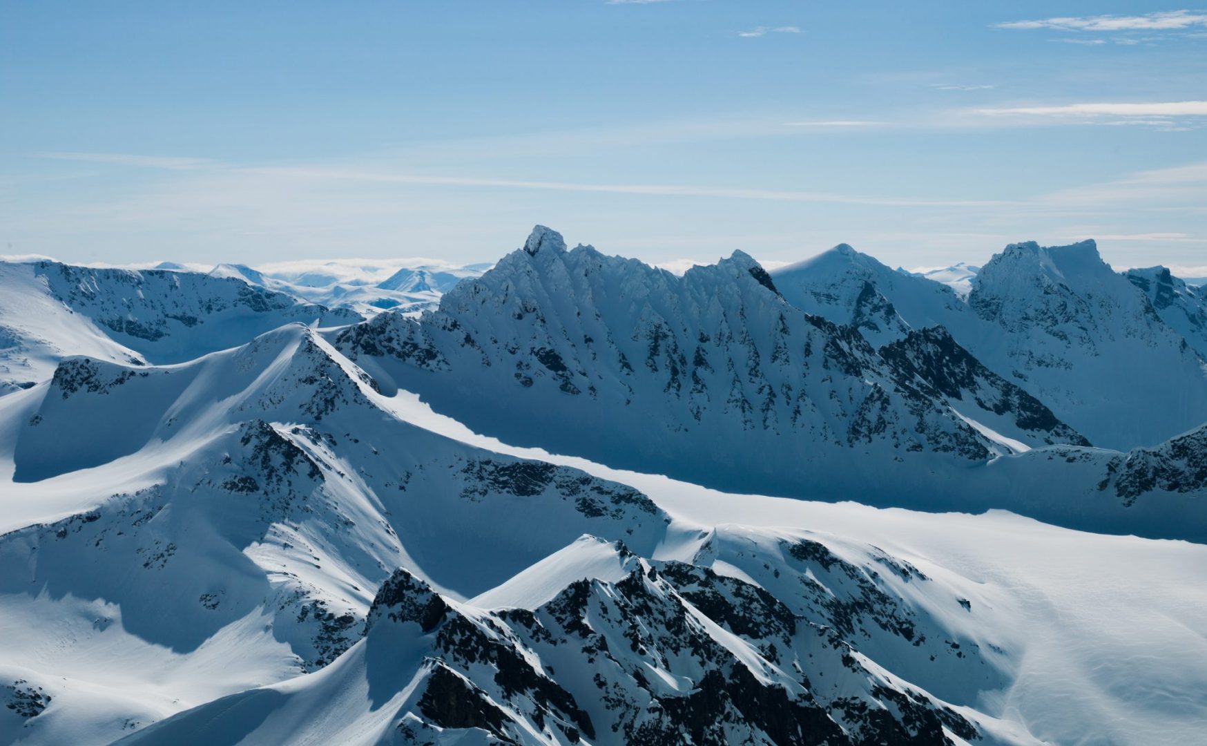 Snødekte fjelltopper under blå himmel.