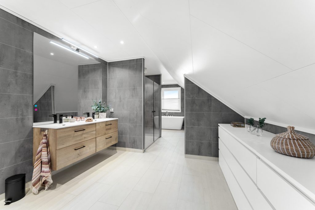 Moderne bad med grå fliser, treinnredning, stor speilflate og dusj.