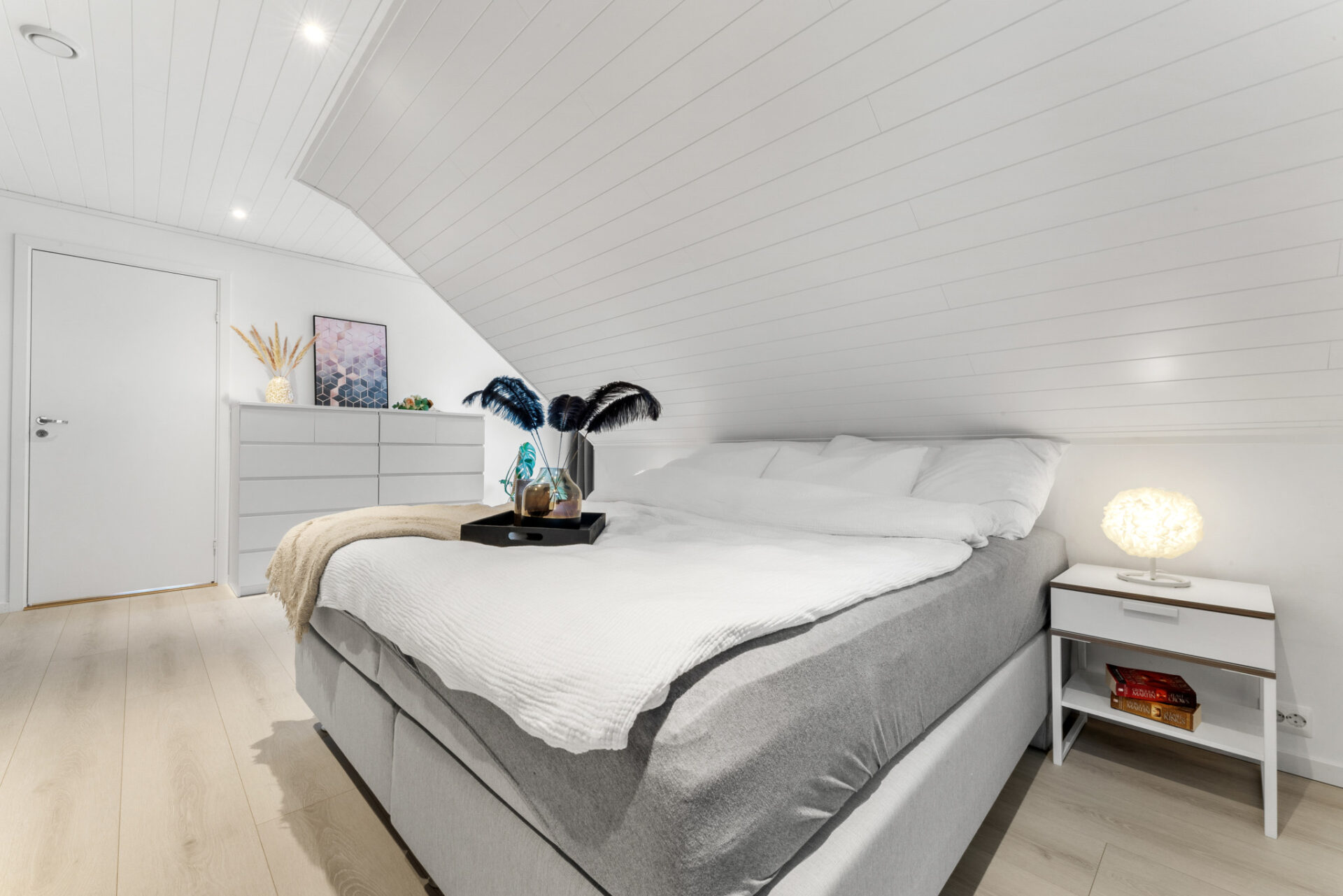 Lyst soverom med dobbeltseng, skråtak og minimalistisk innredning.